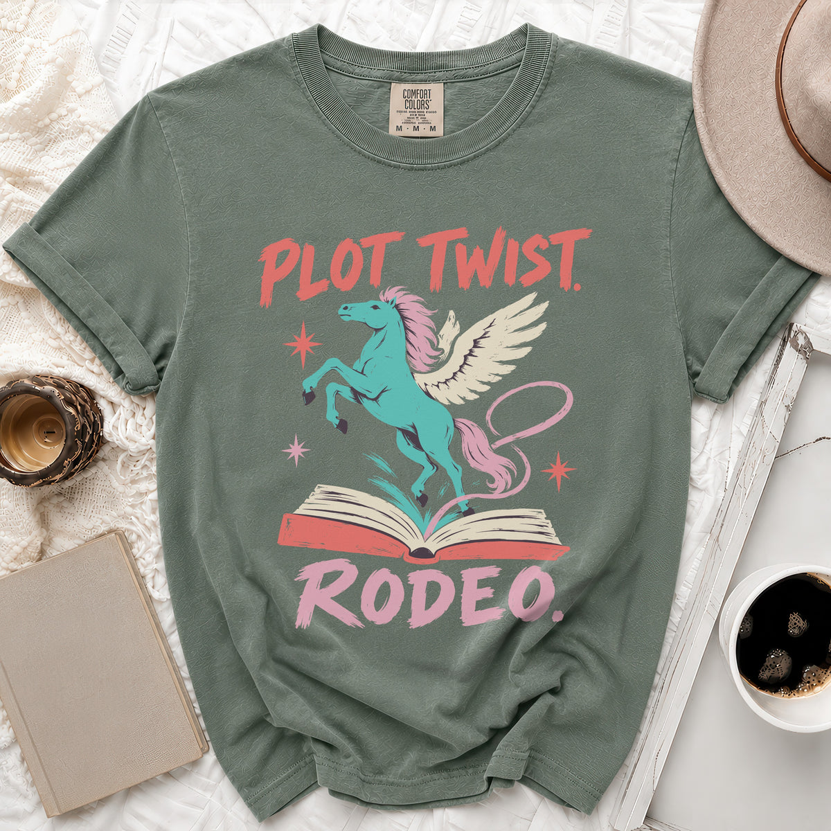 Green t-shirt with "Plot Twist Rodeo" text and winged unicorn on open book.