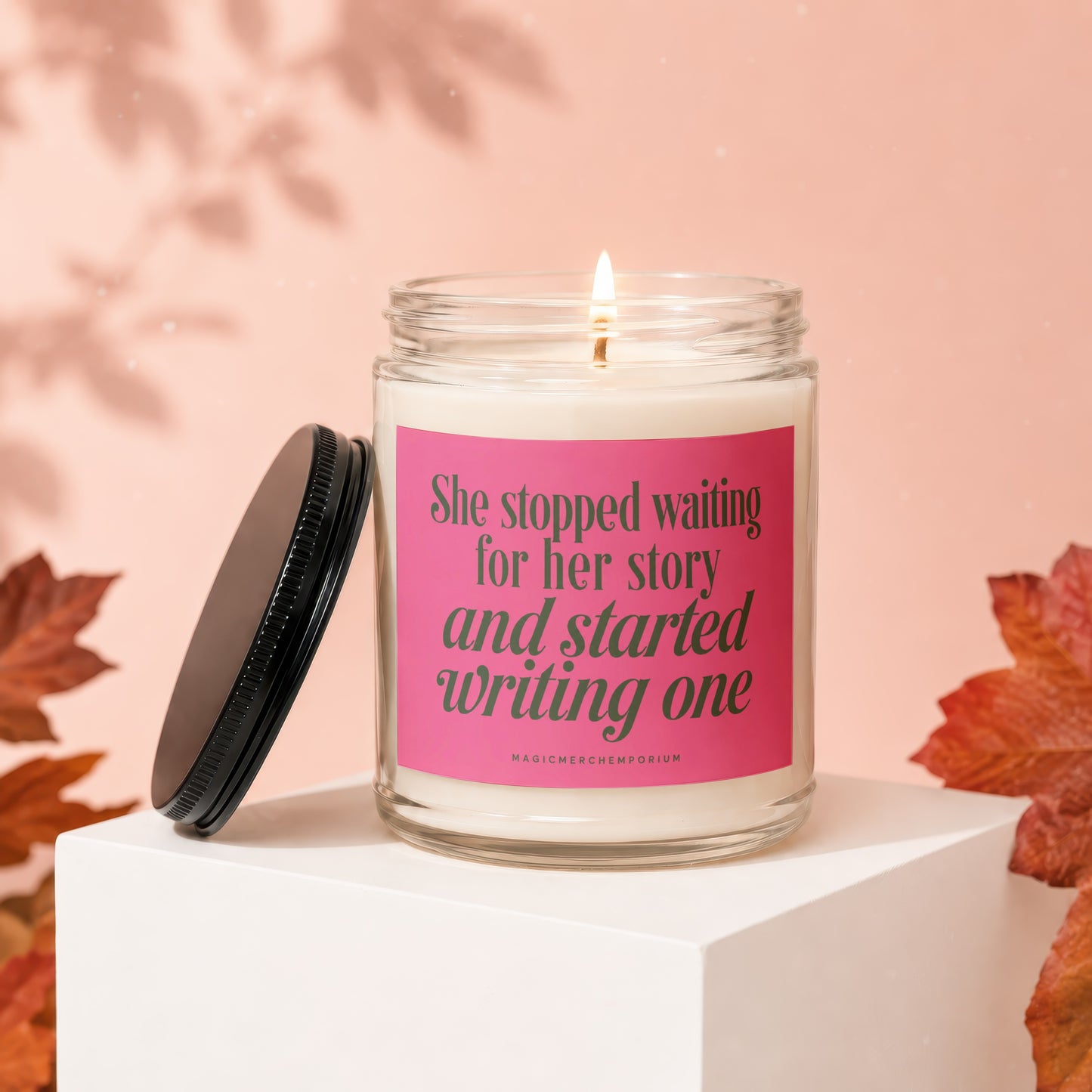 Candle with pink label reading "She stopped waiting for her story and started writing one."