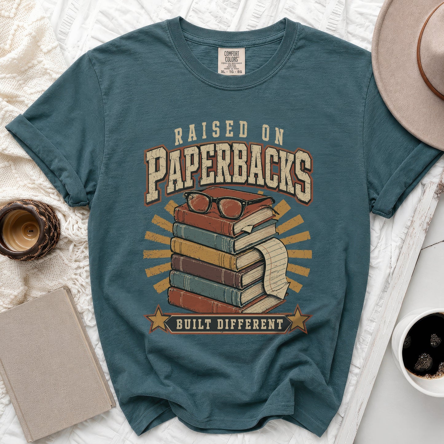 Teal t-shirt with "Raised on Paperbacks Built Different" text and book graphic.