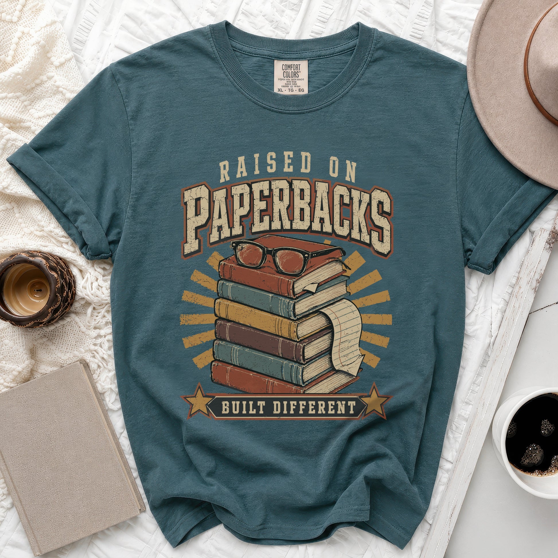 Teal t-shirt with "Raised on Paperbacks Built Different" text and book graphic.