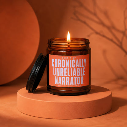 Amber glass candle with lit flame and "Chronically Unreliable Narrator" label.