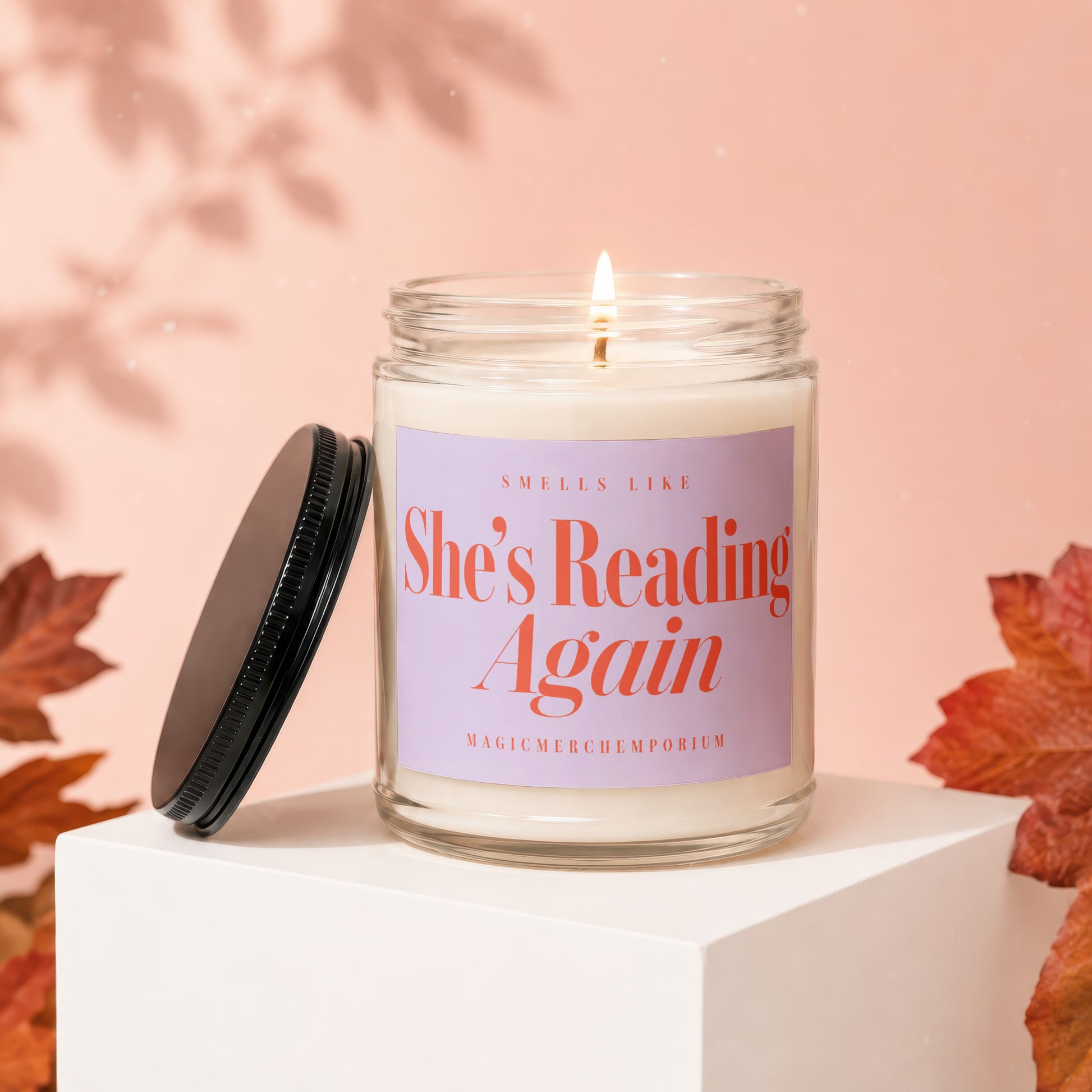 Candle with text "She's Reading Again" on lid and leaves.