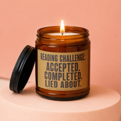 Amber candle with lit wick and black lid, featuring "Reading Challenge: Accepted. Completed. Lied About." text.
