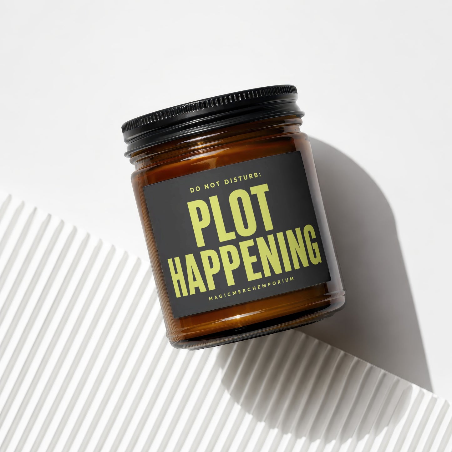 Amber candle in glass jar with black lid and label that reads "DO NOT DISTURB: PLOT HAPPENING".