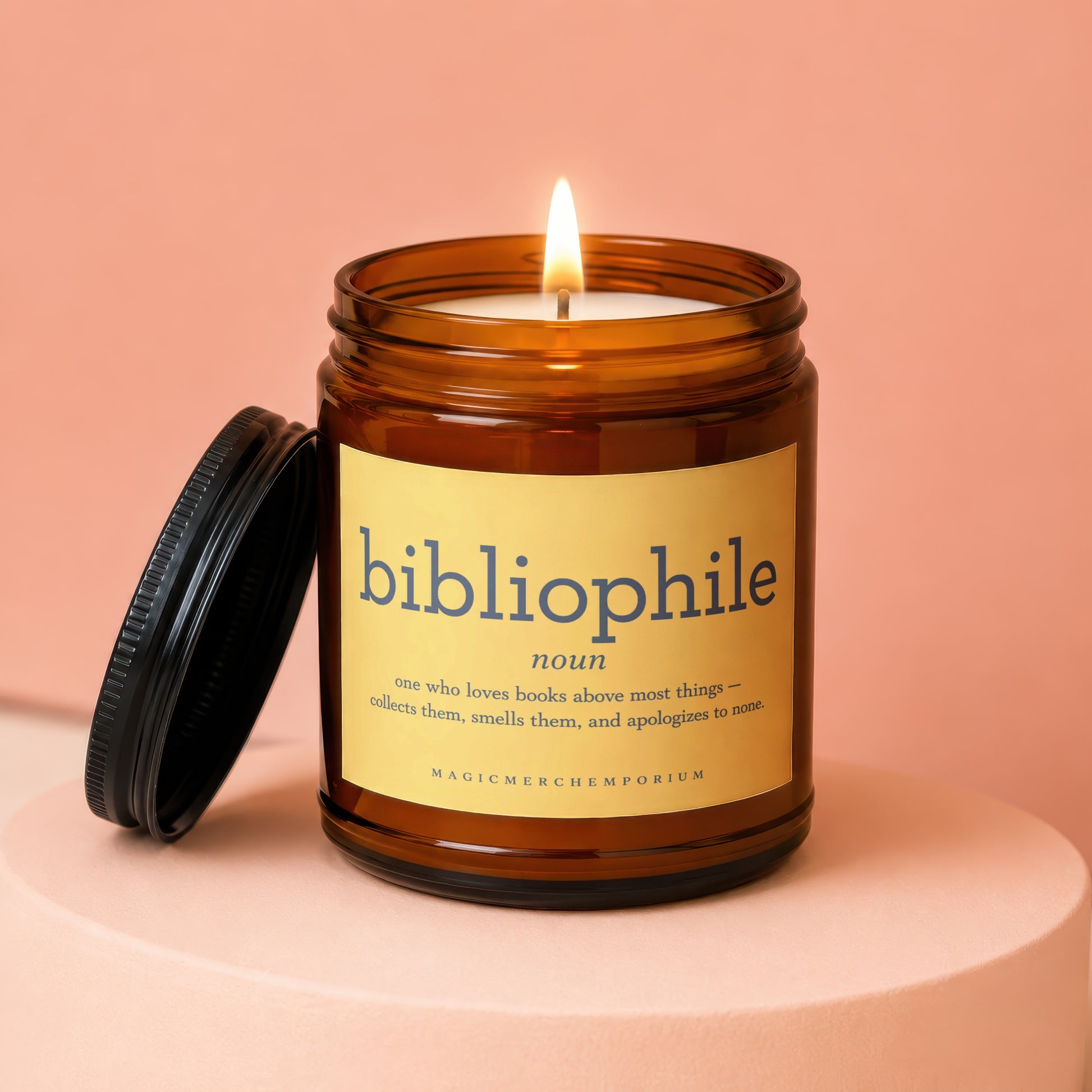 Amber glass candle labeled "bibliophile" with a lit wick, lid off.