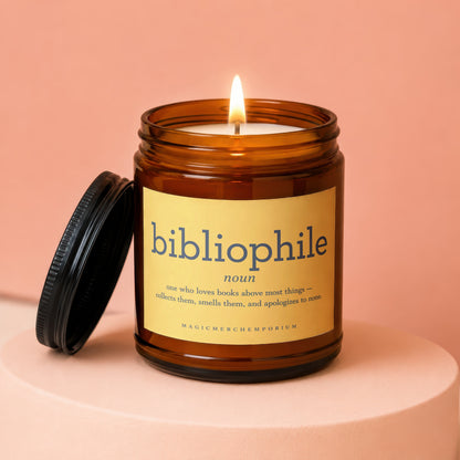 Amber glass candle labeled "bibliophile" with a lit wick, lid off.