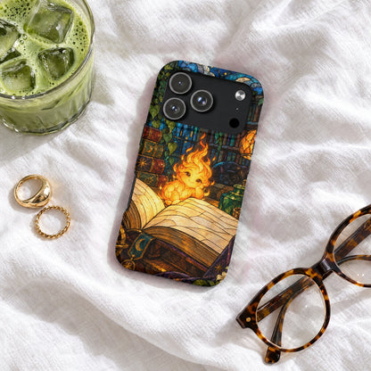 An iPhone case featuring a stained glass design of a fire sprite reading a book, resting on a white blanket with glasses, rings, and a glass of iced matcha.