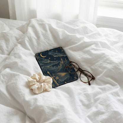 Book with celestial castle design, eyeglasses, and scrunchie on white bedding.