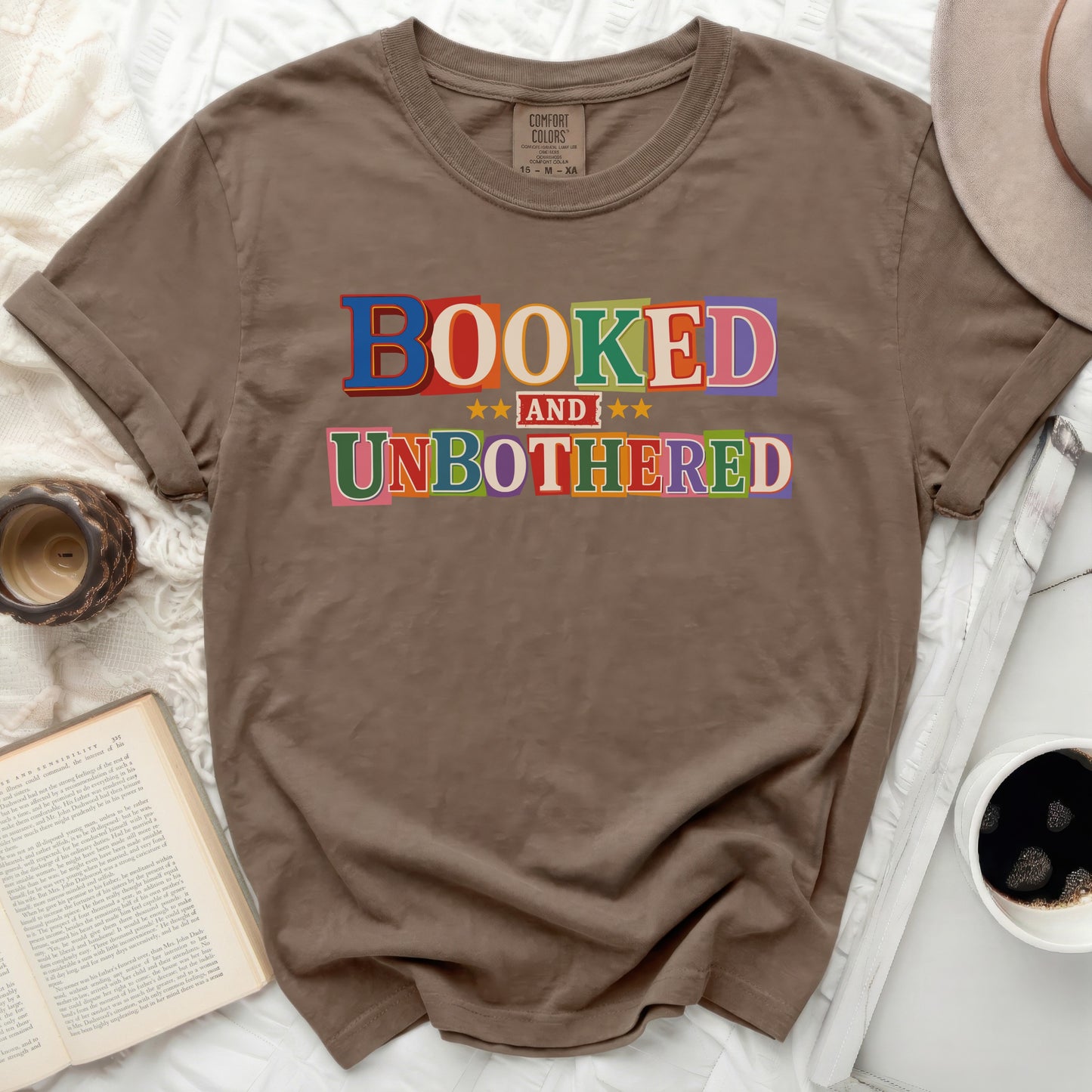 Brown t-shirt with "BOOKED AND UNBOTHERED" text in colorful block letters.