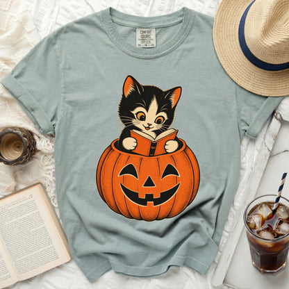 A black and white kitten reads a book sitting inside a jack-o'-lantern.