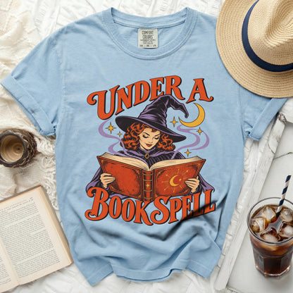 Light blue t-shirt with witch reading book graphic and "Under a Book Spell" text.