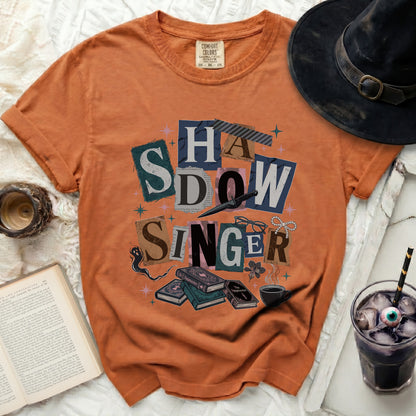Orange t-shirt with "SHADOW SINGER" collage text and Halloween motifs.