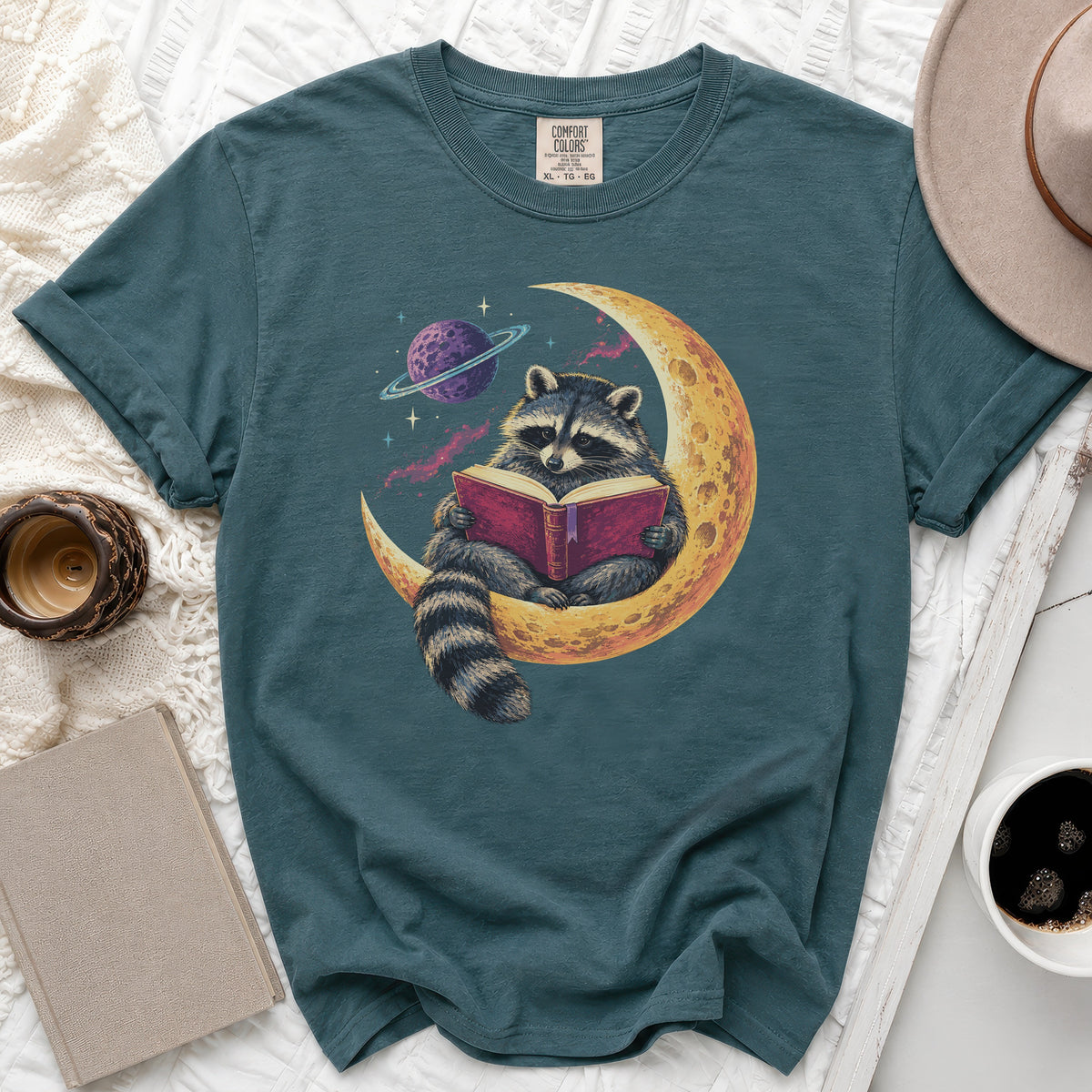 Teal Comfort Colors t-shirt with raccoon reading book on moon graphic.