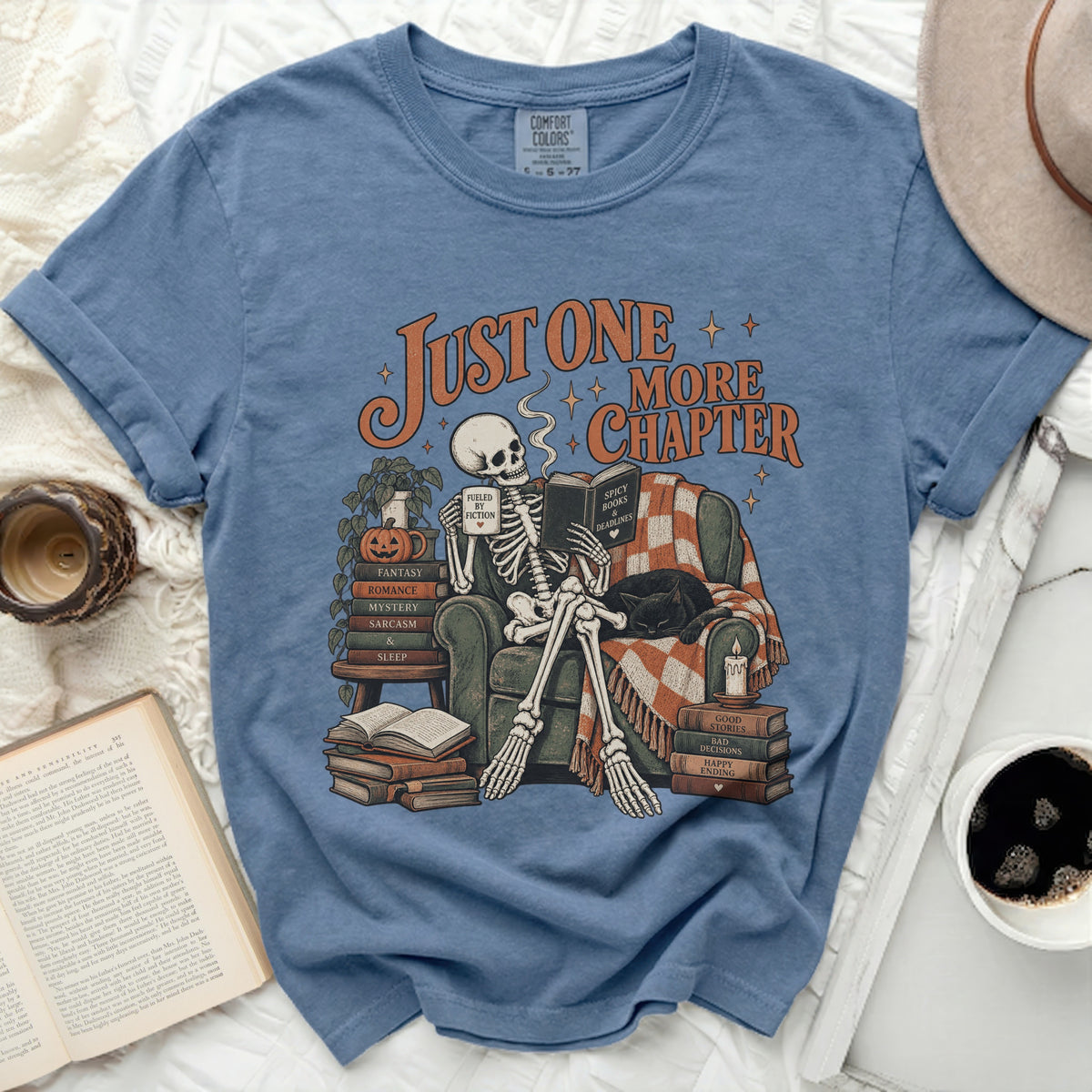 Skeleton reading a book with text "Just One More Chapter" on blue t-shirt.