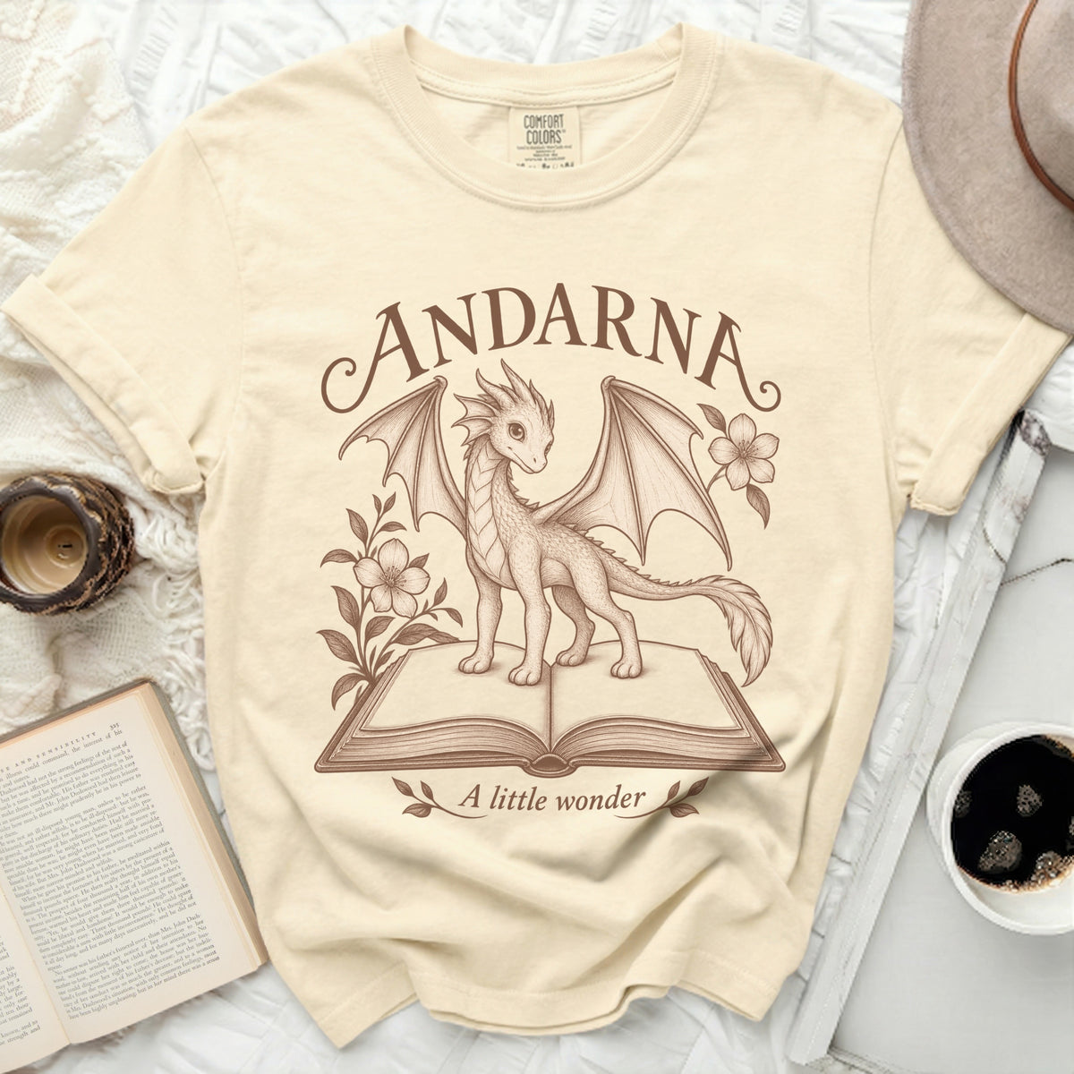 Cream t-shirt with a sketch of a dragon on an open book, text "ANDARNA" and "A little wonder".