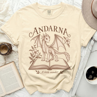 Cream t-shirt with a sketch of a dragon on an open book, text "ANDARNA" and "A little wonder".