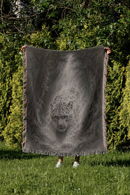 A person is standing in a grassy area, holding up a large black and white blanket that features a detailed image of a leopard's face.