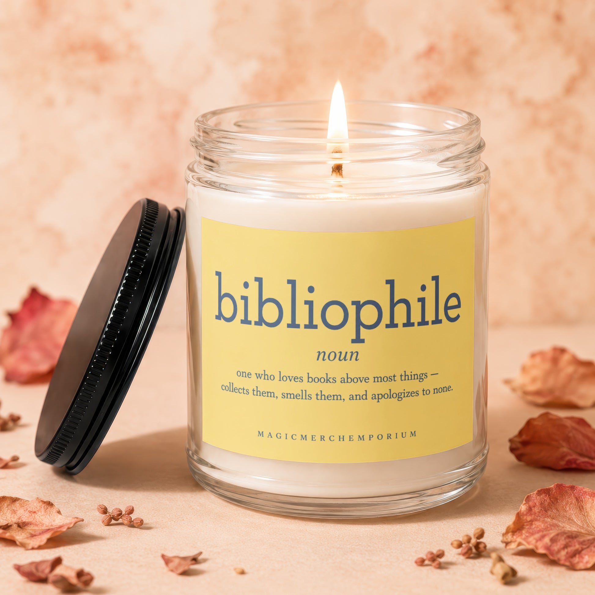 A lit candle in a jar with a yellow label that says "bibliophile noun [...] MAGICMERCHEMPORIUM"