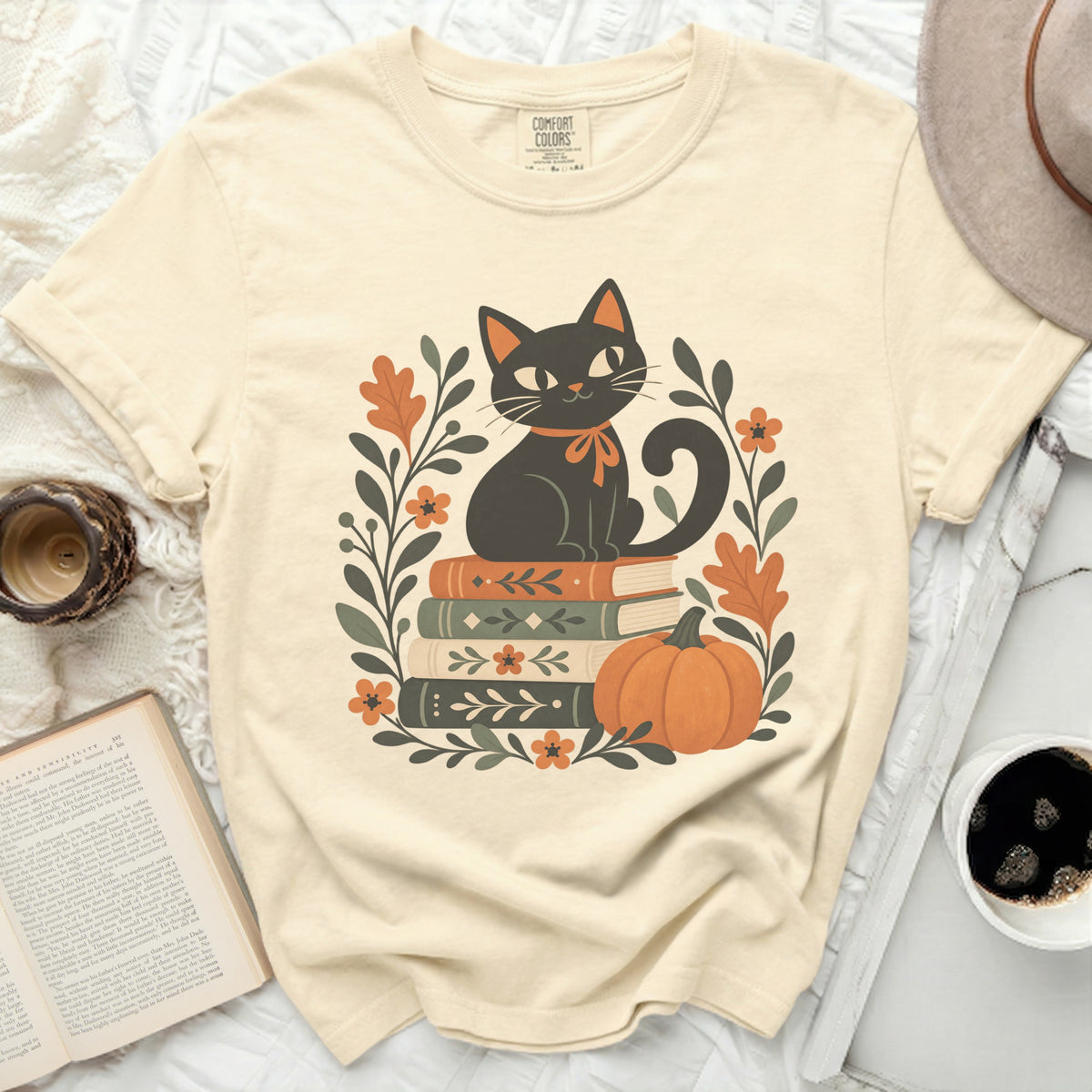 Black cat sitting on books with pumpkin and floral border on cream t-shirt.