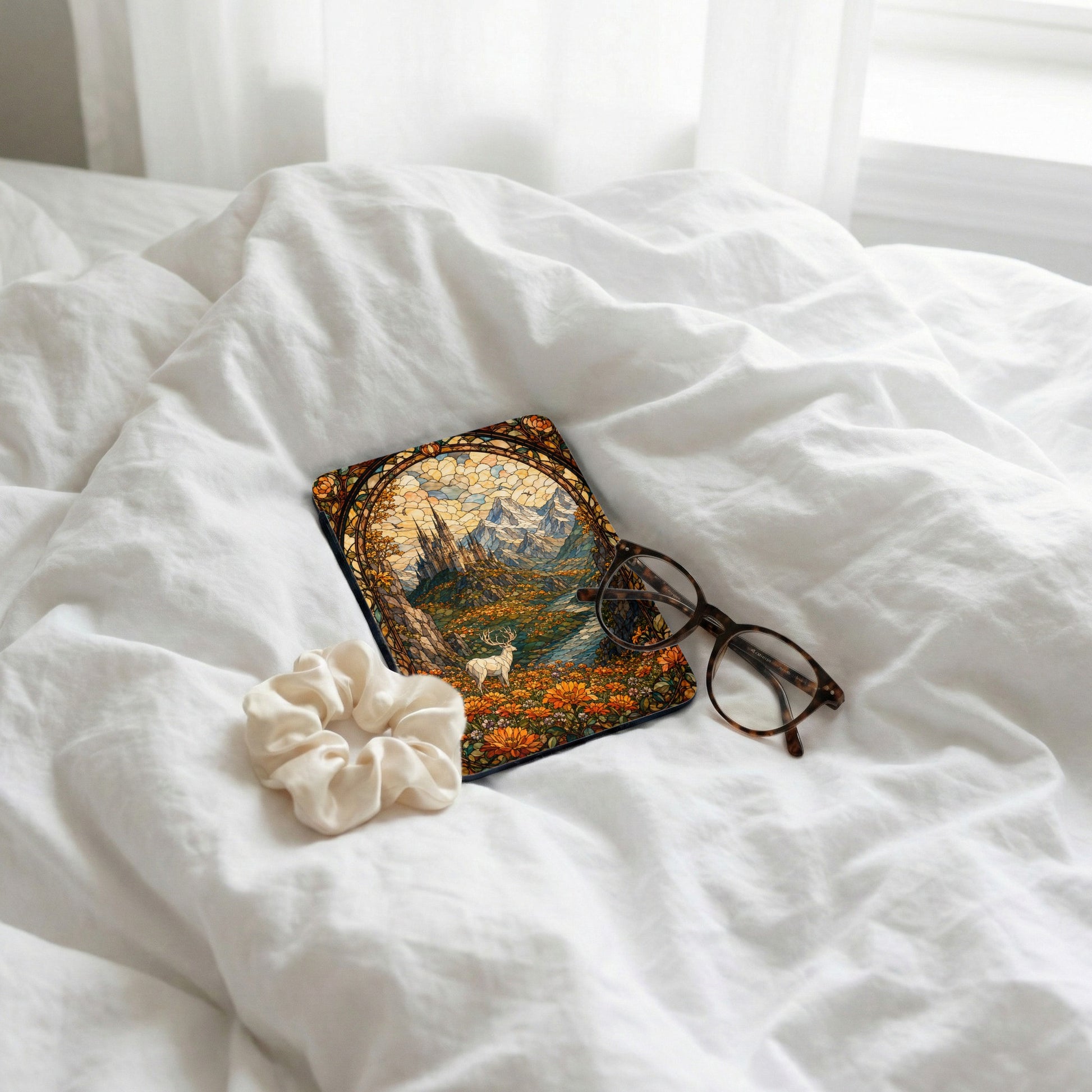 Case with stained glass art, including a deer, castle, and mountains, placed on crumpled white sheets.