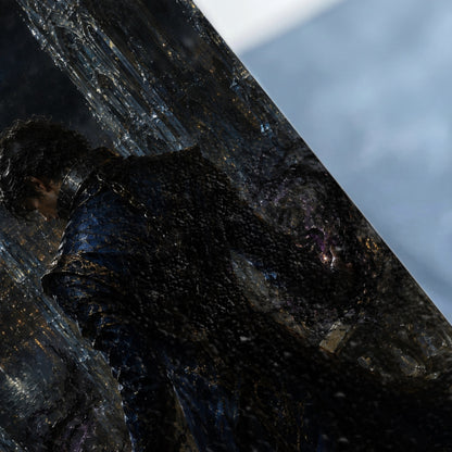 Man in dark patterned armor looking down, reflected in textured black and blue surface.