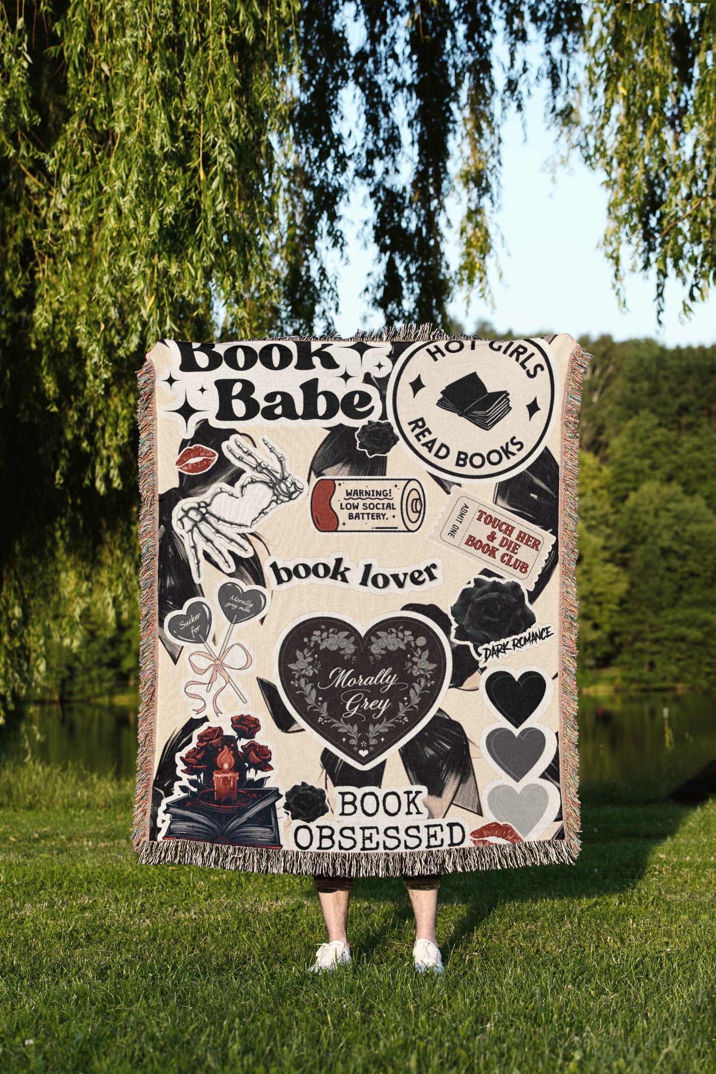 A person is standing in a grassy area, holding a blanket that is decorated with various book-related designs and text.