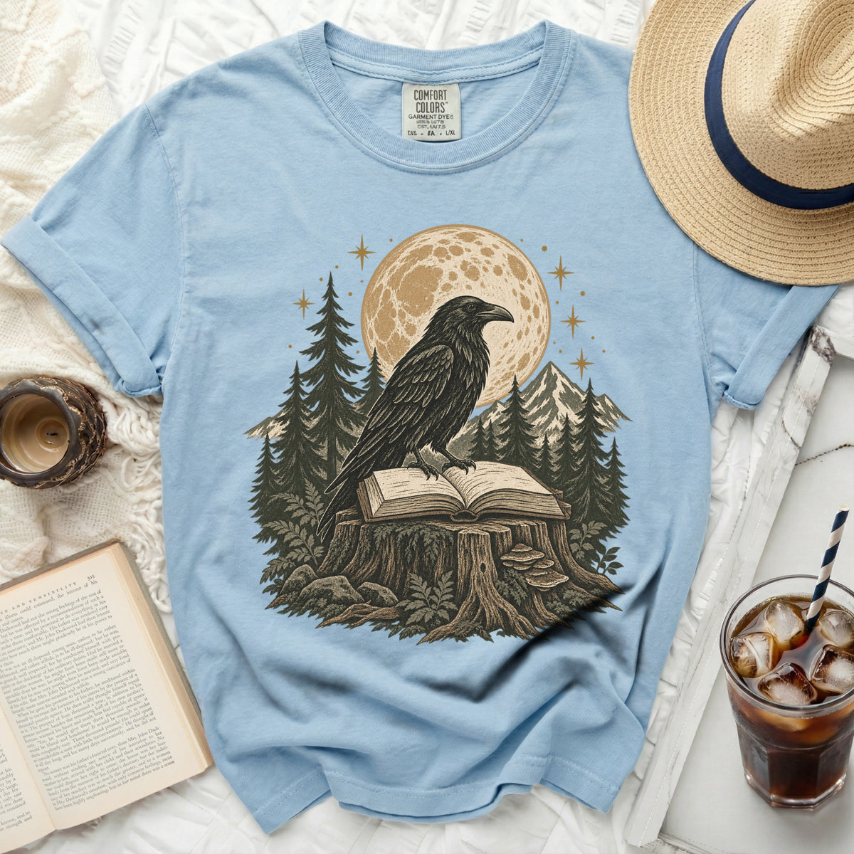 Light blue t-shirt with a raven on an open book on a tree stump design.