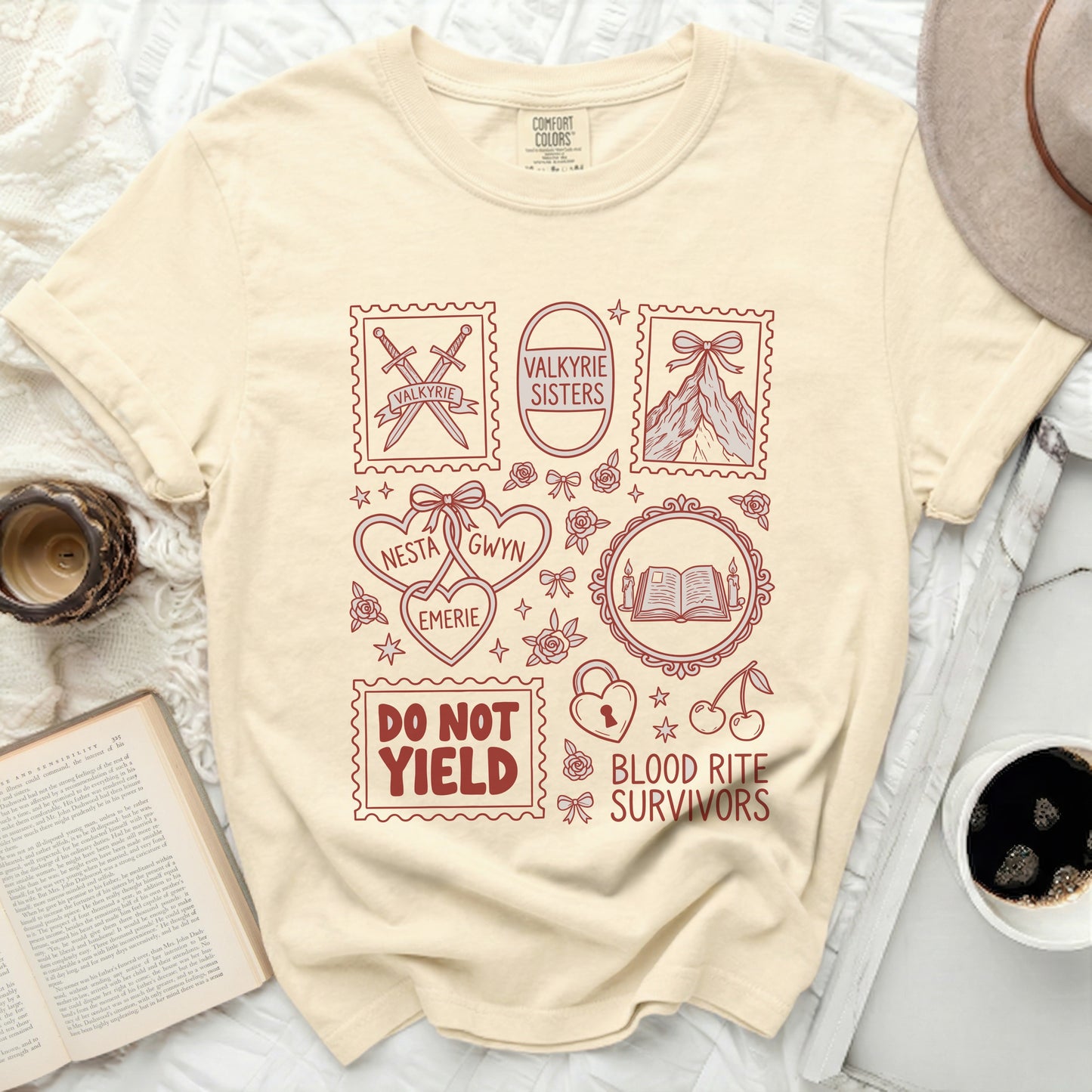 Cream t-shirt with red graphic of stamps, swords, mountains, books, hearts, and text.