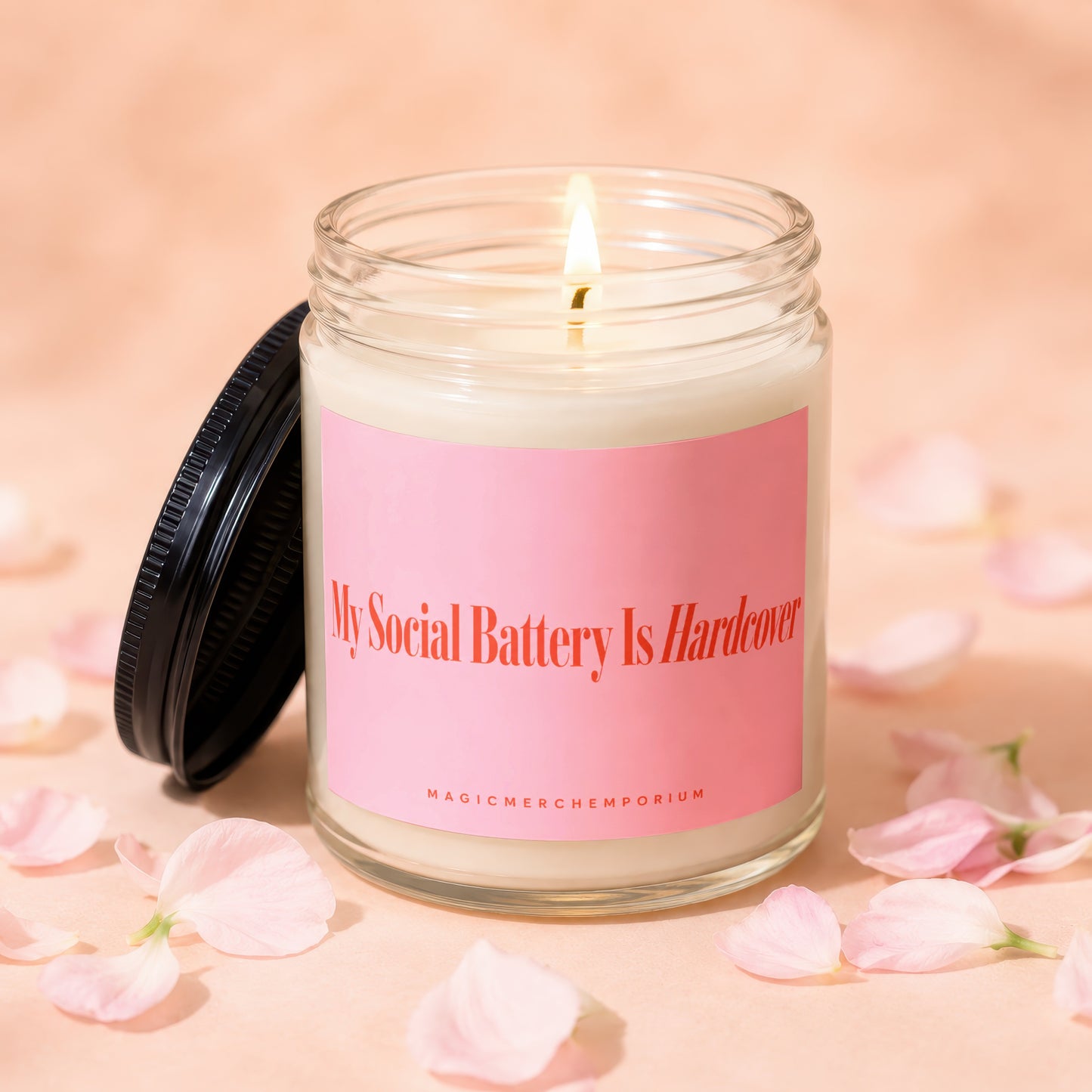 Glass candle with lit wick and pink label saying "My Social Battery Is Hardcover".