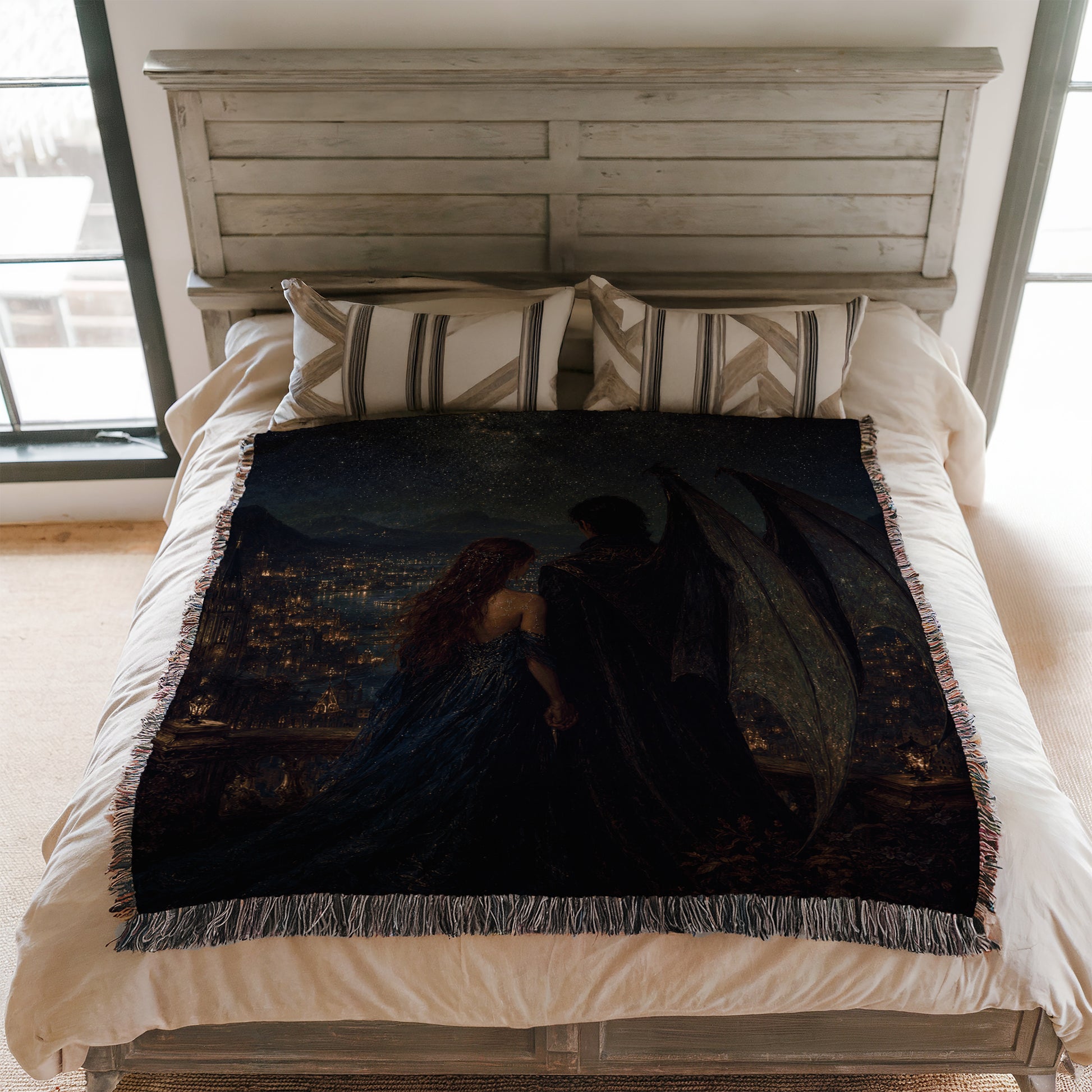 a bedroom with a bed featuring a large, dark-colored blanket with a painting of a woman and a man on it. The bed is set against a white wooden headboard, and there are pillows on the bed.