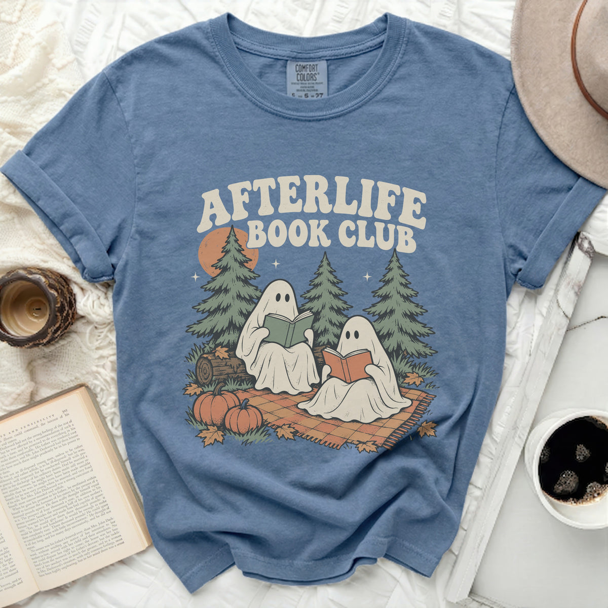 Two ghosts read books on a blanket with pumpkins and trees.