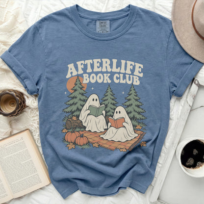 Two ghosts read books on a blanket with pumpkins and trees.