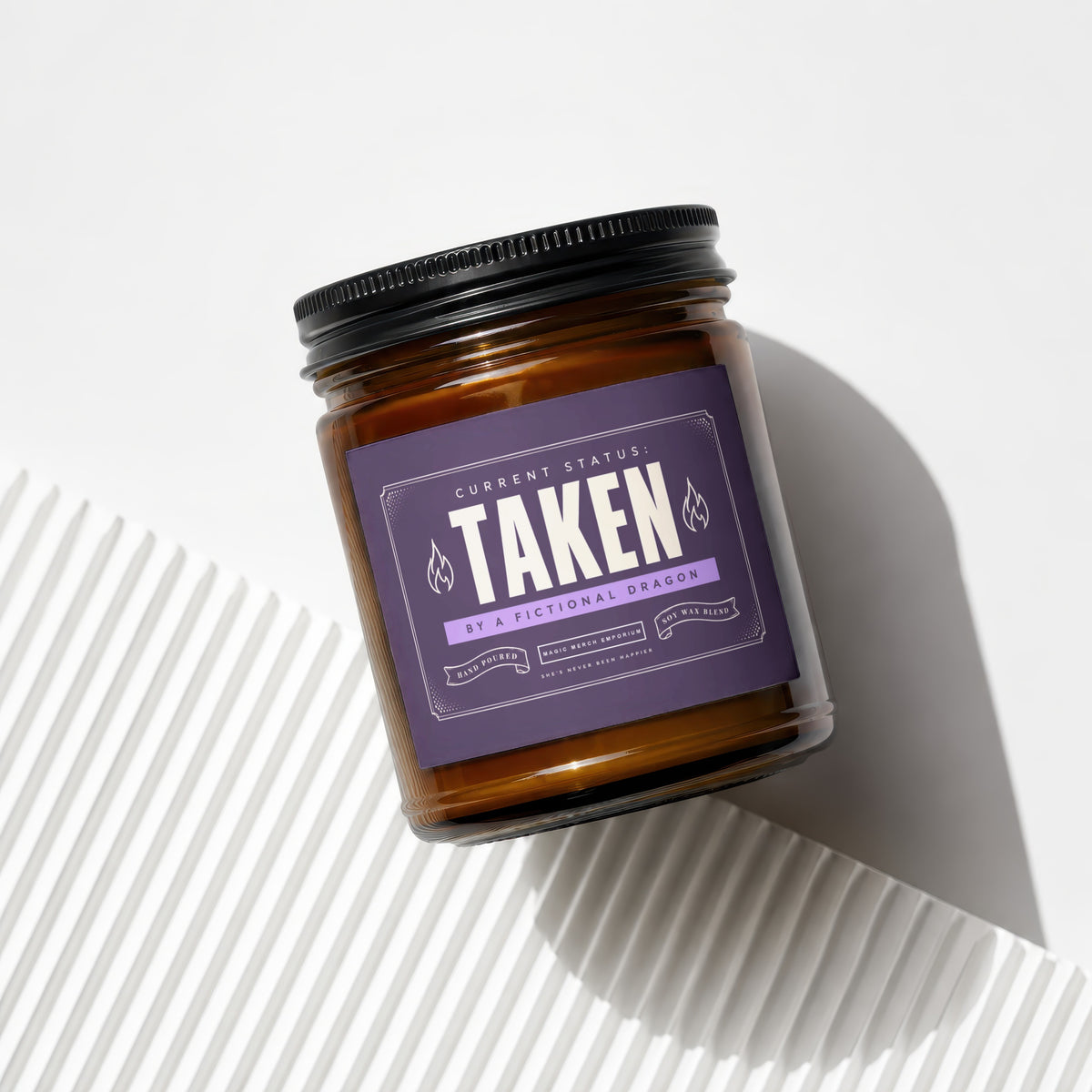 Amber glass candle with purple label reading "Taken by a Fictional Dragon."