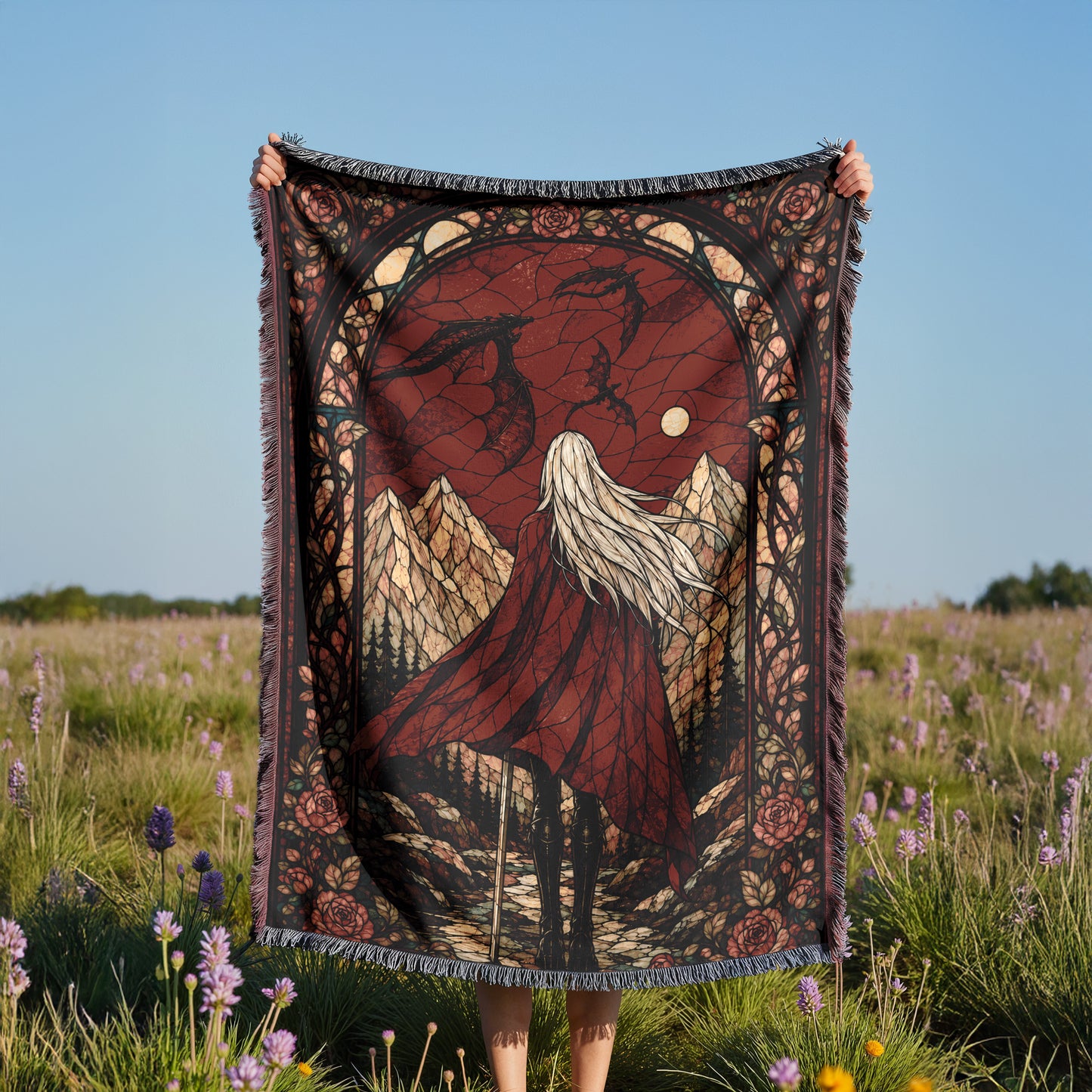 A person is holding up a large, ornate blanket with a detailed design of a woman with long hair and a flowing red dress, set against a backdrop of mountains and a clear sky.