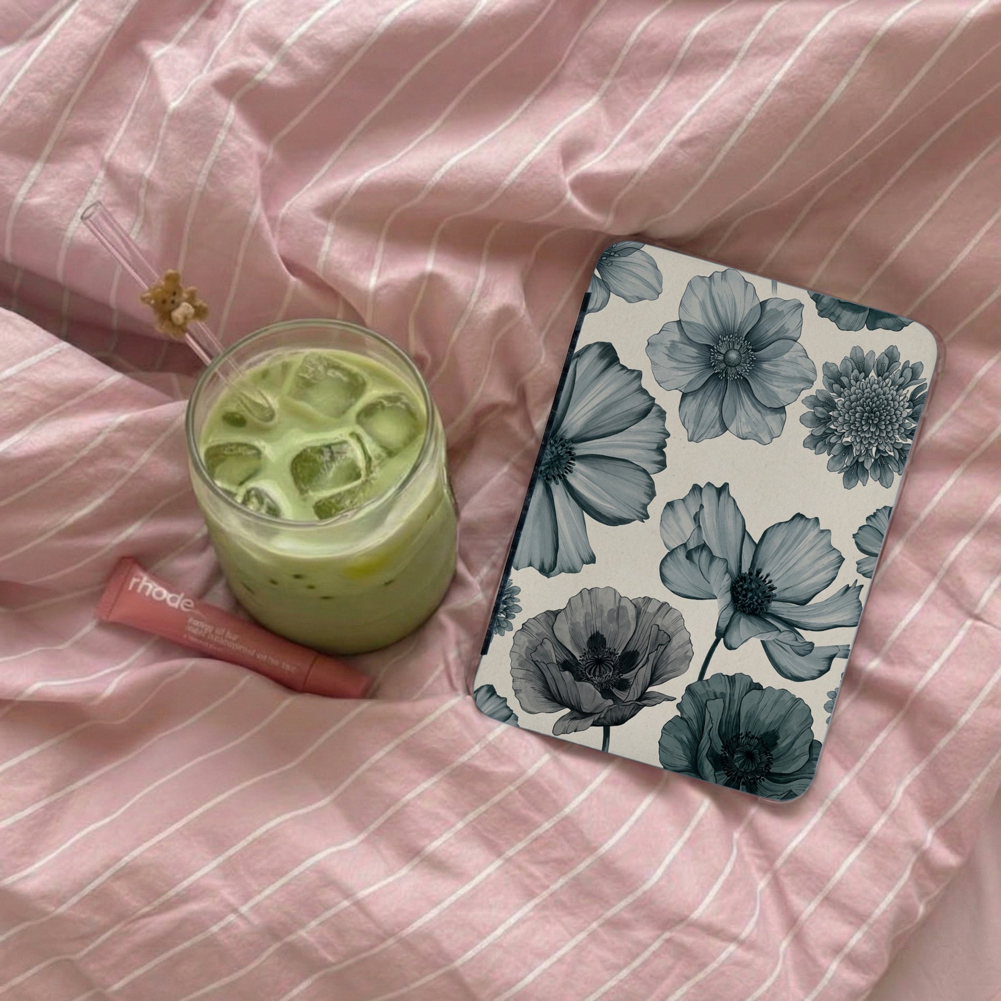 Phone case with floral pattern beside drink and lip balm on pink striped fabric.
