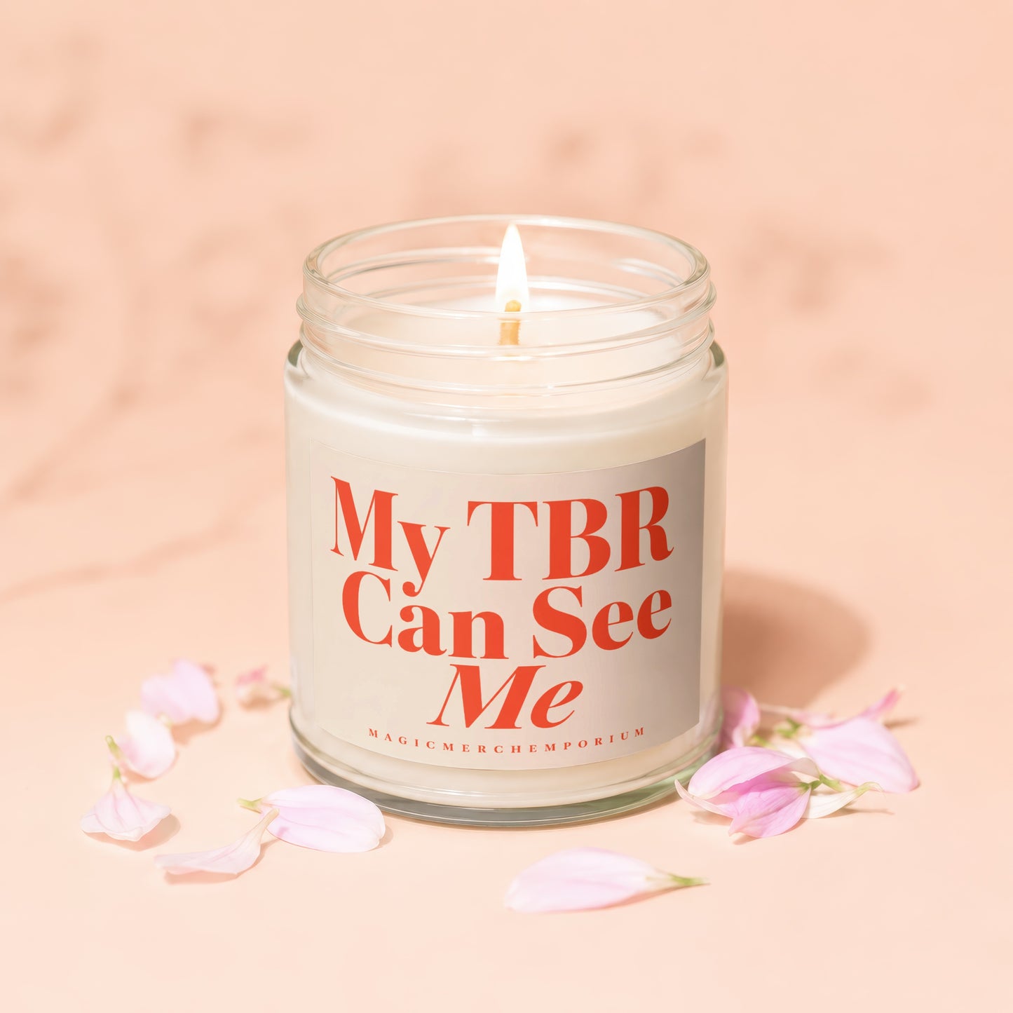 Candle with text "My TBR Can See Me" and a lit wick, surrounded by pink petals.