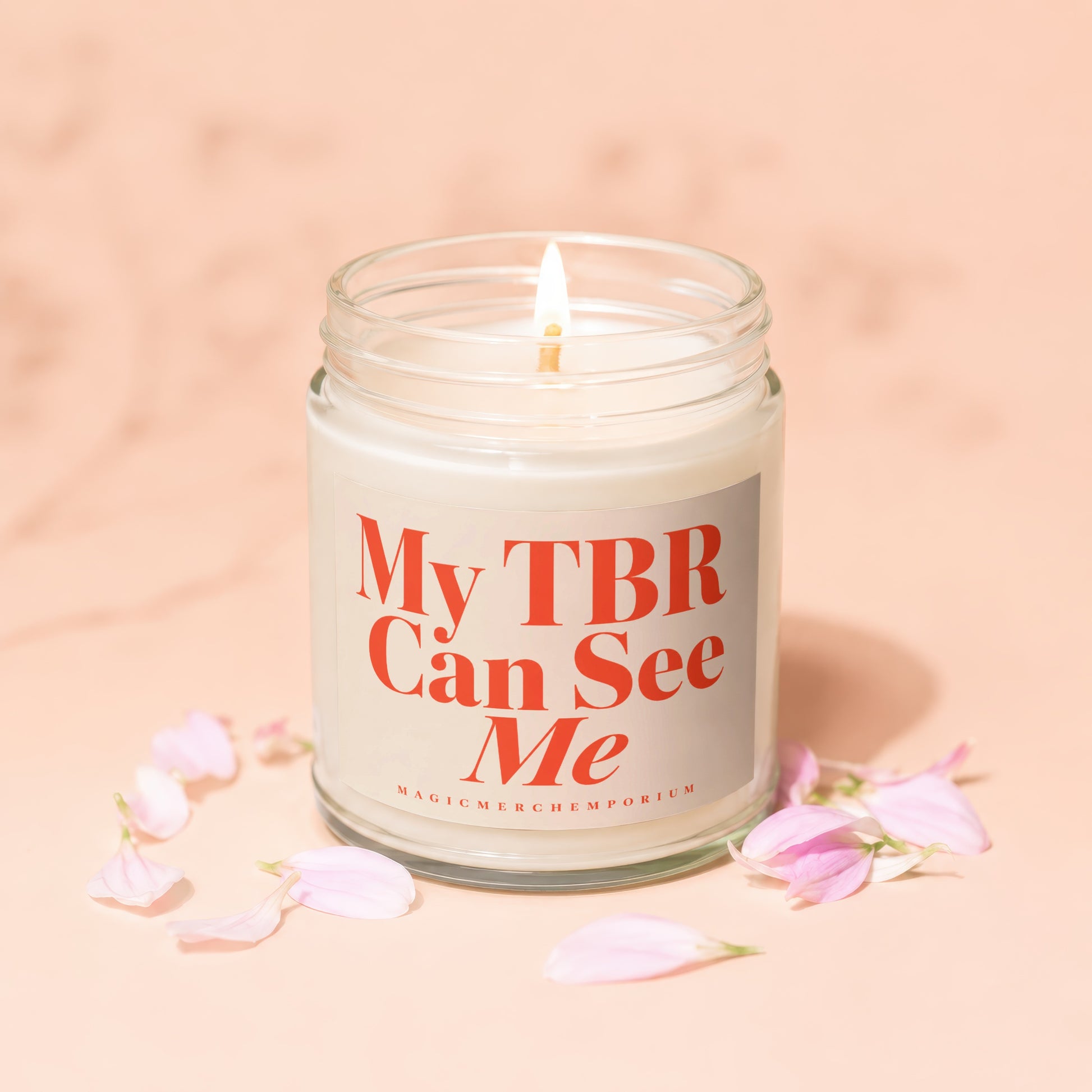 Candle with text "My TBR Can See Me" and a lit wick, surrounded by pink petals.