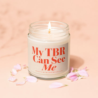 Candle with text "My TBR Can See Me" and a lit wick, surrounded by pink petals.