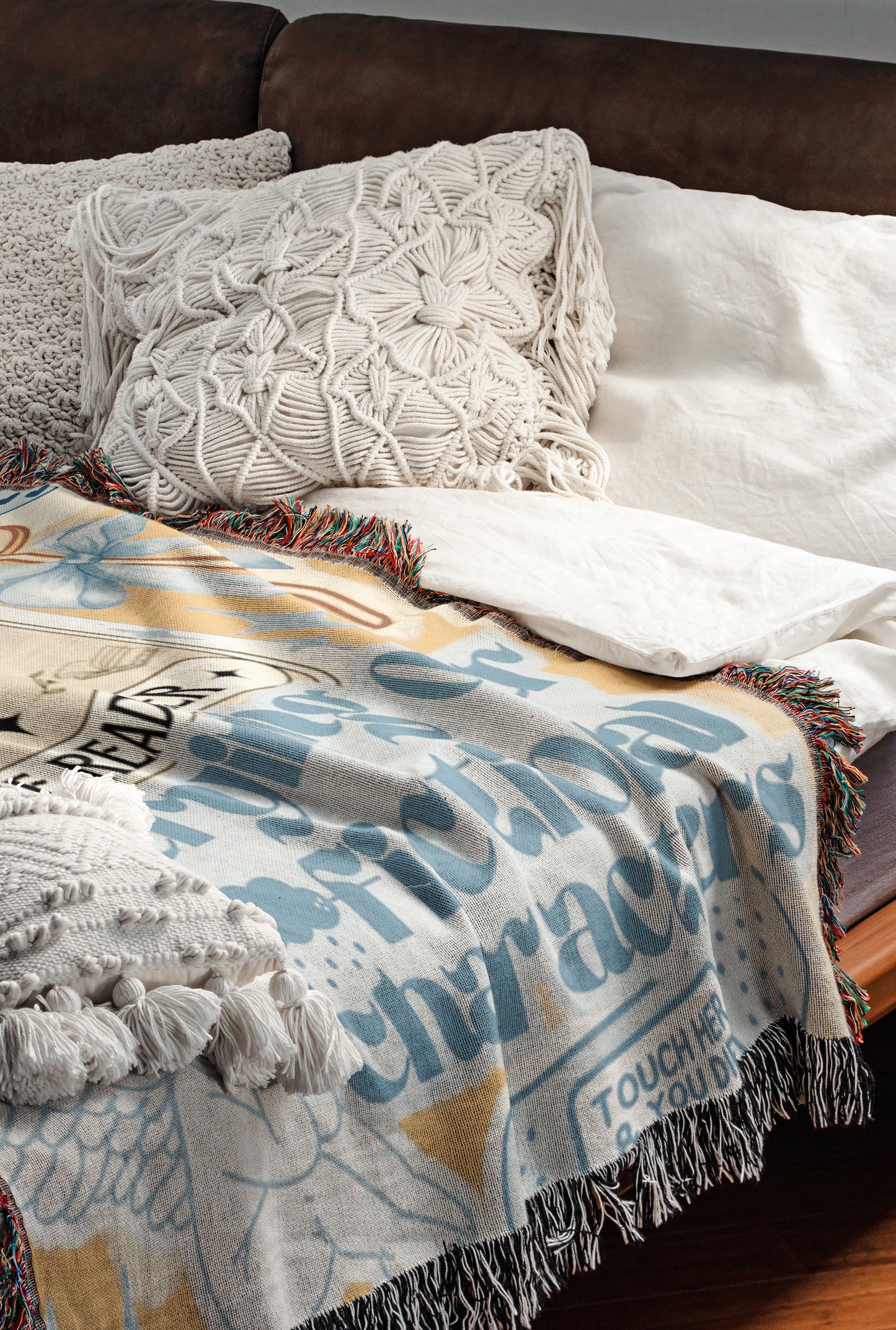 a cozy and inviting bedroom scene, featuring a comfortable bed with a colorful blanket and pillows. The bed is covered with a white comforter and has a wooden headboard. The blanket has a unique design with a mix of blue, white, and yellow colors, and it is adorned with fringe details. The pillows are arranged neatly, adding to the overall aesthetic of the room.