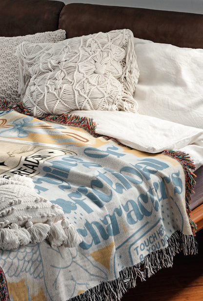 a cozy and inviting bedroom scene, featuring a comfortable bed with a colorful blanket and pillows. The bed is covered with a white comforter and has a wooden headboard. The blanket has a unique design with a mix of blue, white, and yellow colors, and it is adorned with fringe details. The pillows are arranged neatly, adding to the overall aesthetic of the room.
