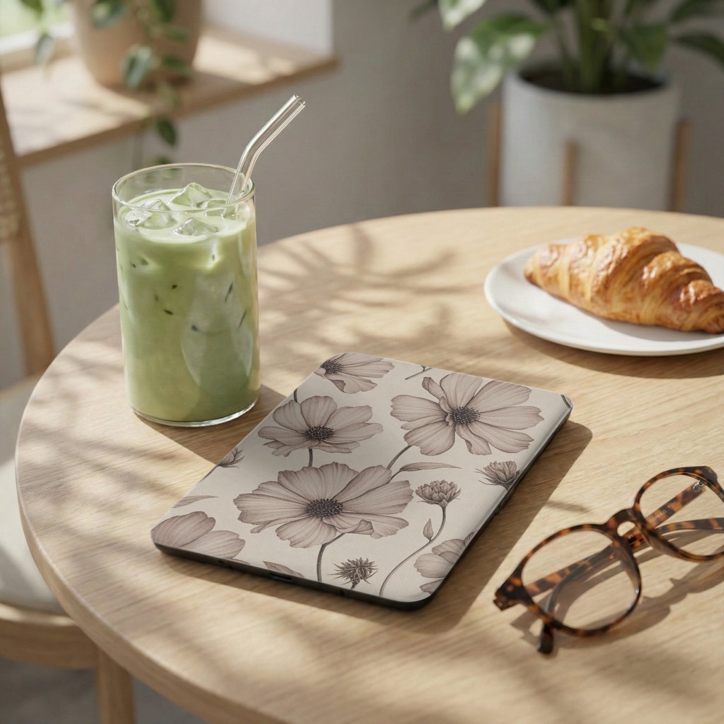 Floral patterned tablet case next to iced matcha, croissant, and glasses.