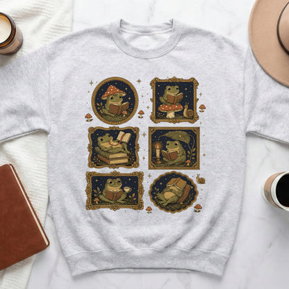 Grey sweatshirt with six framed illustrations of frogs reading books among mushrooms and stars.