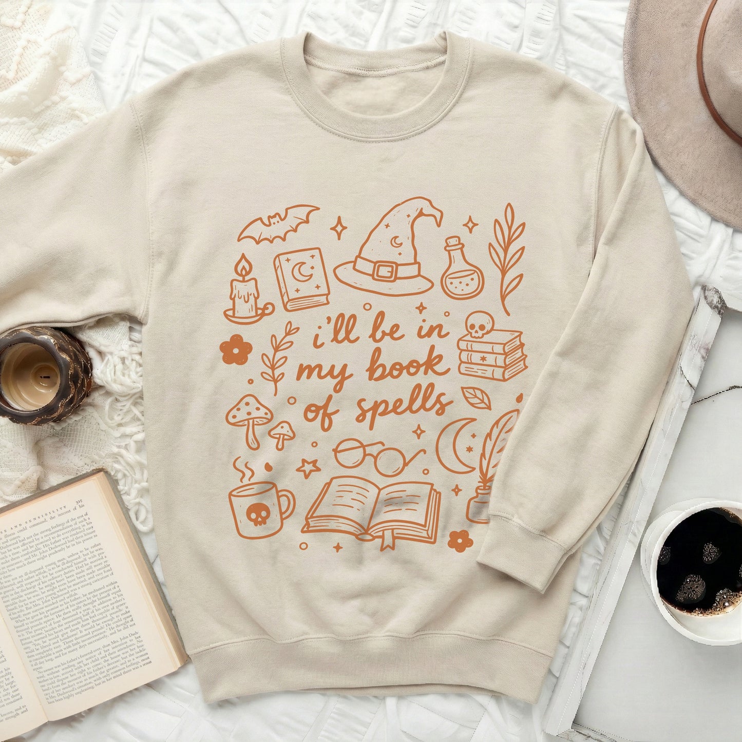 Cream sweatshirt with orange witchy icons and "i'll be in my book of spells" text.