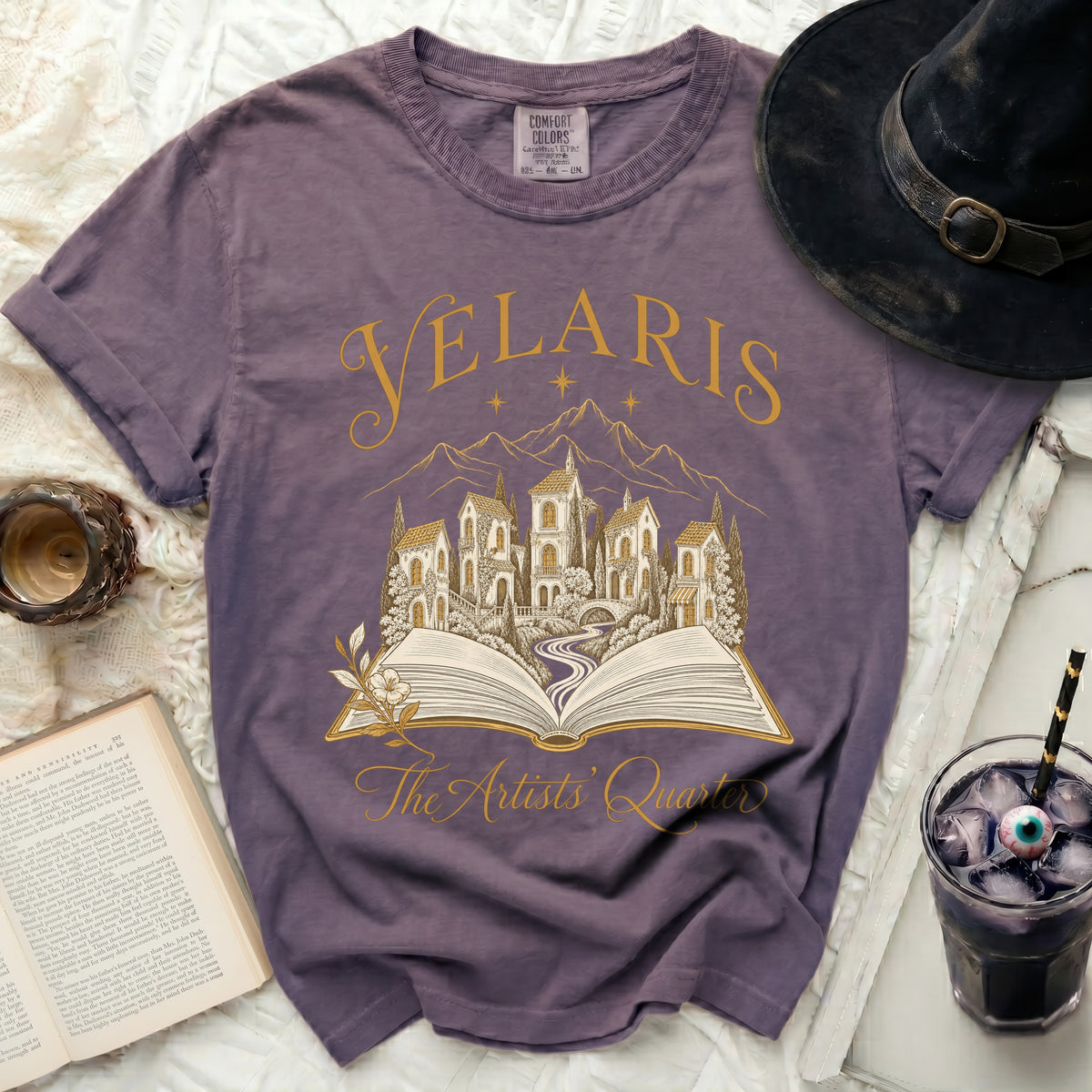 Purple t-shirt with gold text "Velaris The Artists' Quarter" and an open book illustration.