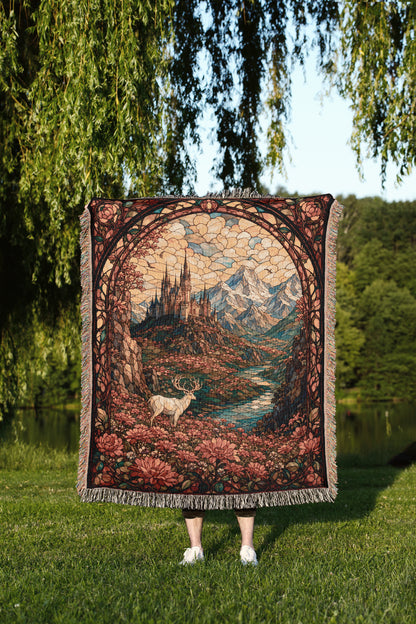 A person is standing in a grassy area, holding a large, ornate tapestry or blanket that features a castle, mountains, and a deer.