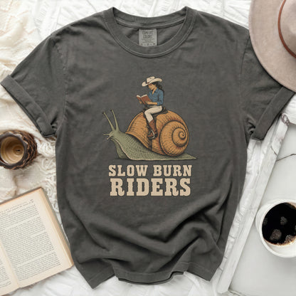 T-shirt graphic with cowgirl reading on a snail and text "SLOW BURN RIDERS".