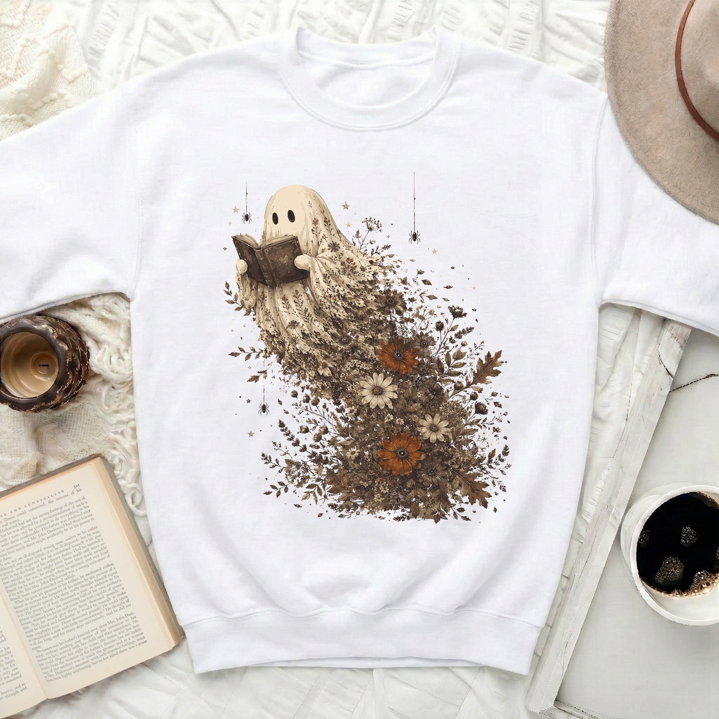 White crewneck sweatshirt featuring a ghost character reading a book surrounded by flowers.
