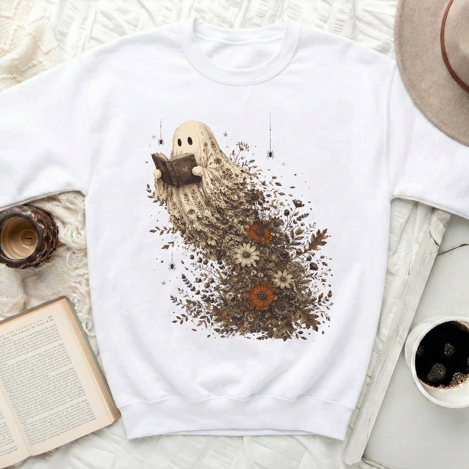 White crewneck sweatshirt featuring a ghost character reading a book surrounded by flowers.