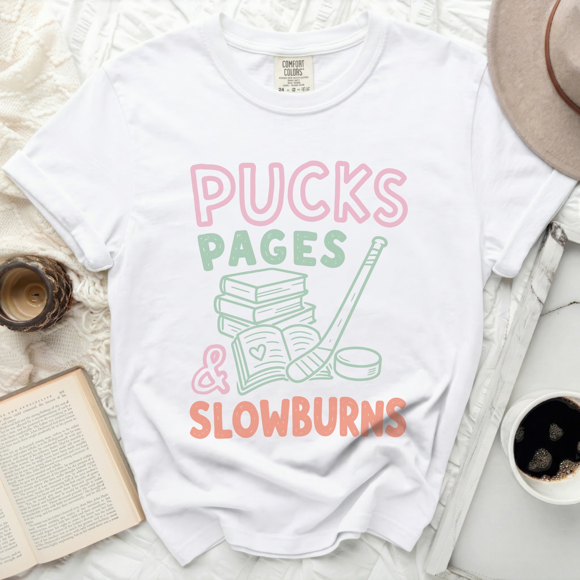 White t-shirt with "Pucks Pages & Slowburns" in pink and green.