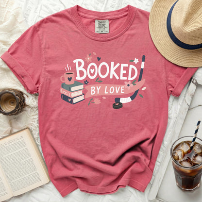 Pink t-shirt with "Booked by Love" text and books, hockey stick, and heart graphic.